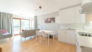 A modern, well-lit living room with a sofa, a dining table, and a kitchen area.