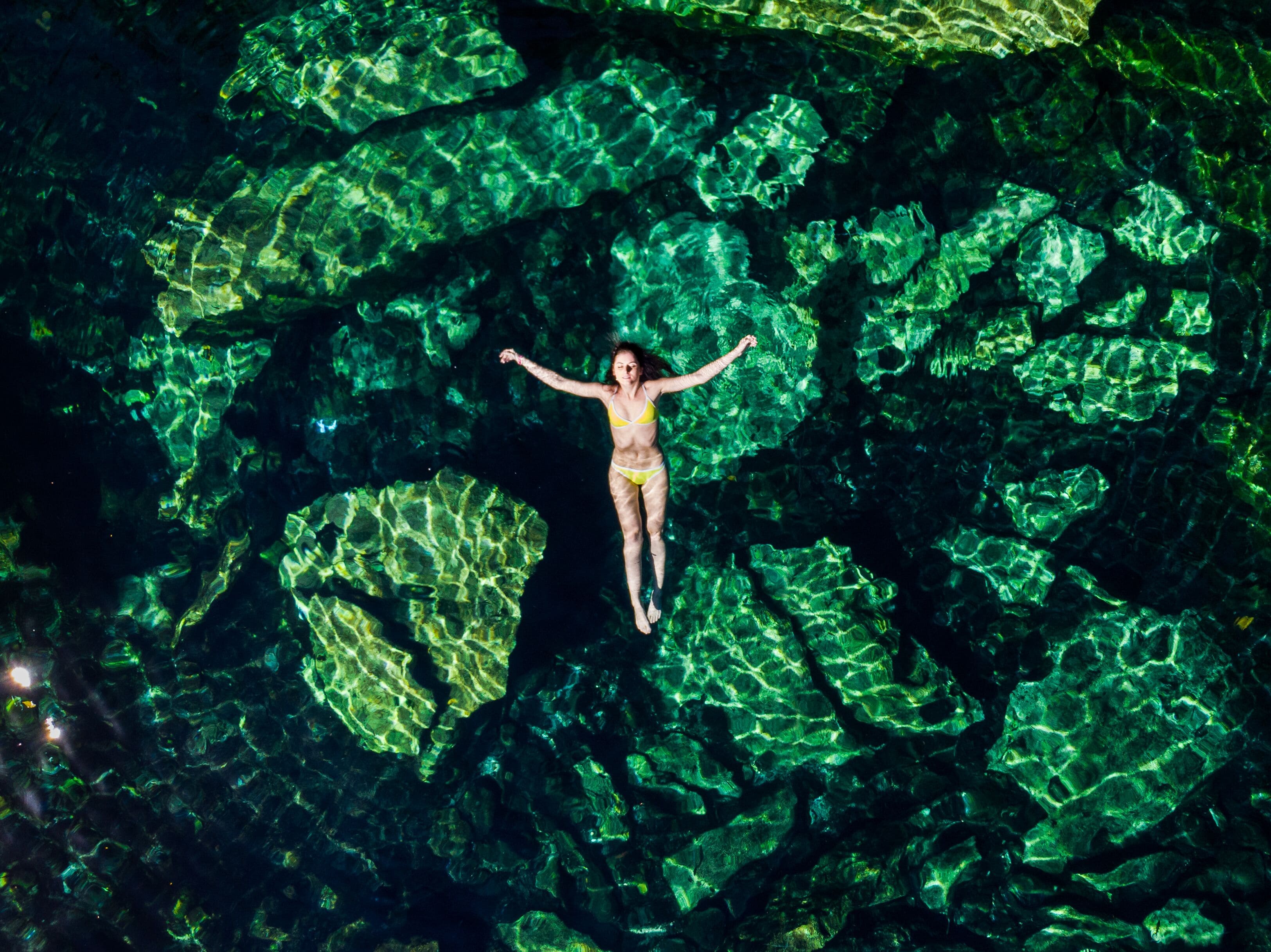 A person floating in a cave with large, green crystalline formations.