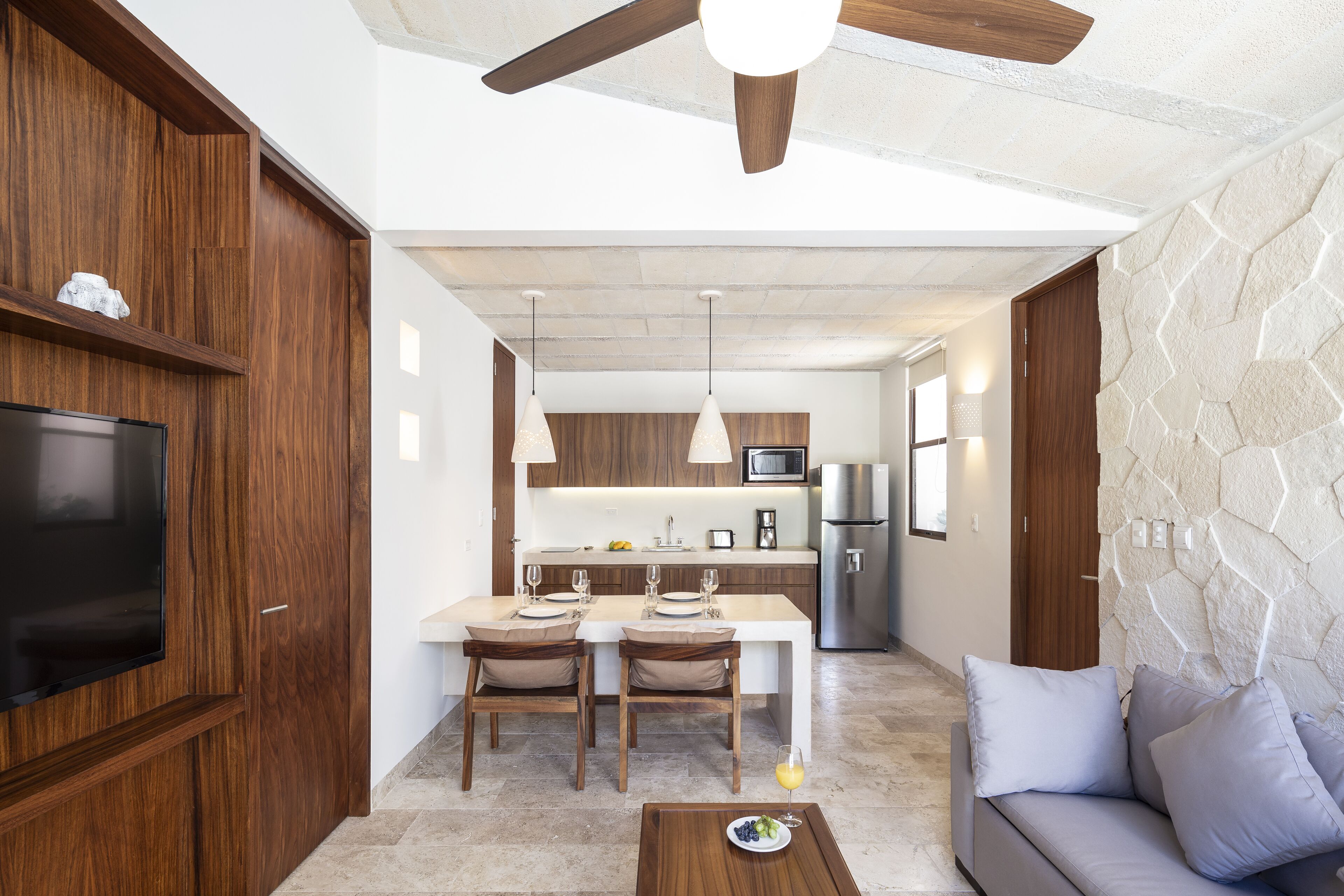 A modern kitchen with wooden cabinets, a dining area with two chairs, a sofa, and a TV.