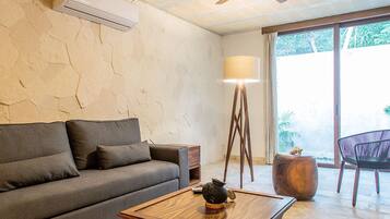 Un salón con un sofá gris, una mesa de centro de madera, una lámpara de pie y vistas a zonas verdes al exterior.