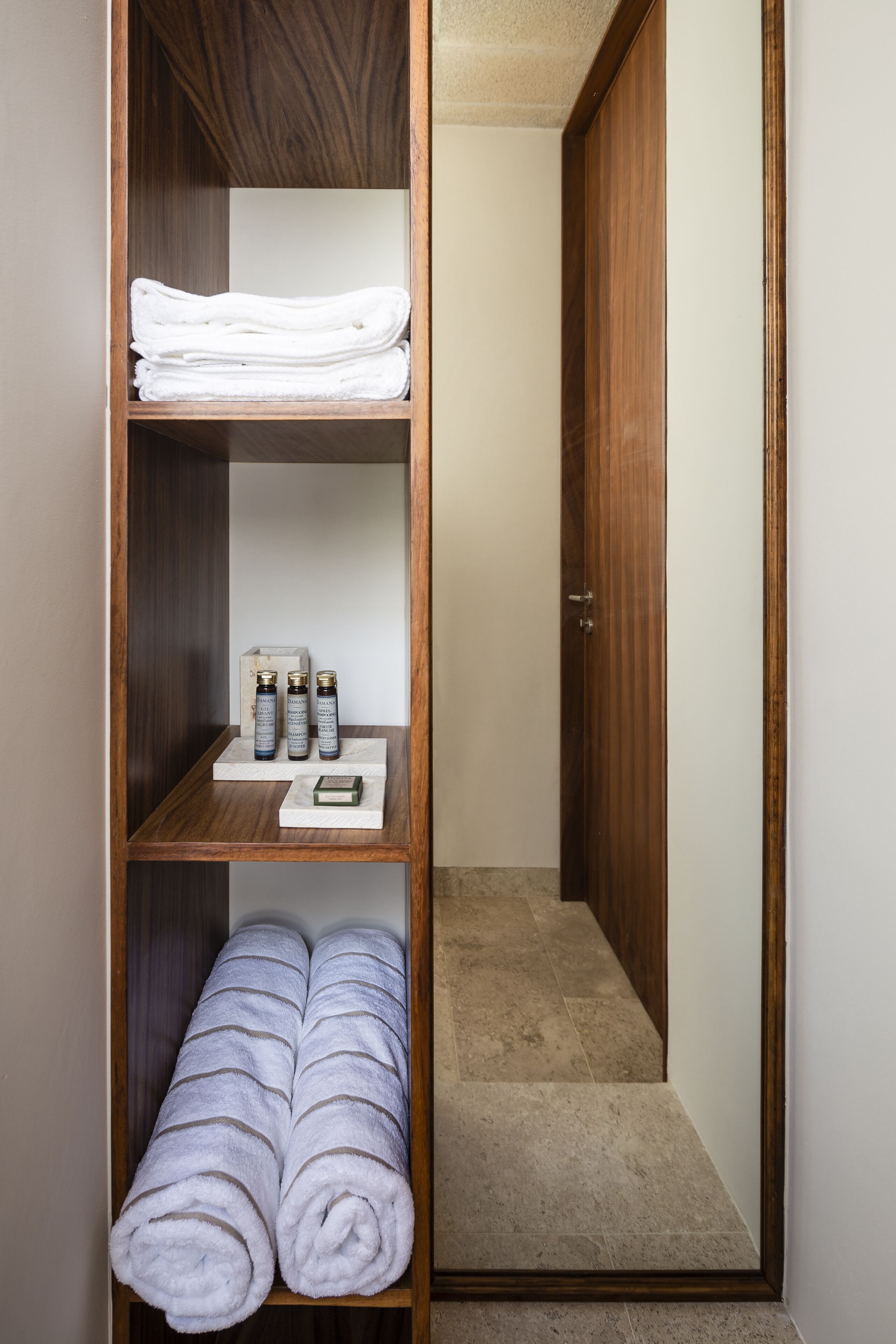 A wooden wardrobe with folded white towels and toiletries.