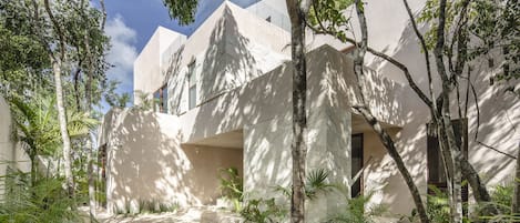 Un edificio moderno con fachada geométrica, rodeado de abundante vegetación y un sendero de grava.