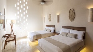 A modern bedroom with two beds, a ceiling fan, and a wall with small windows. - Kiki Tulum (Tulum)