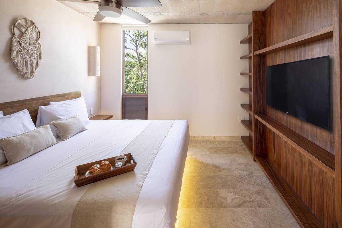 A bedroom with a bed, a tray with croissants, a ceiling fan, and a TV mounted on the wall.