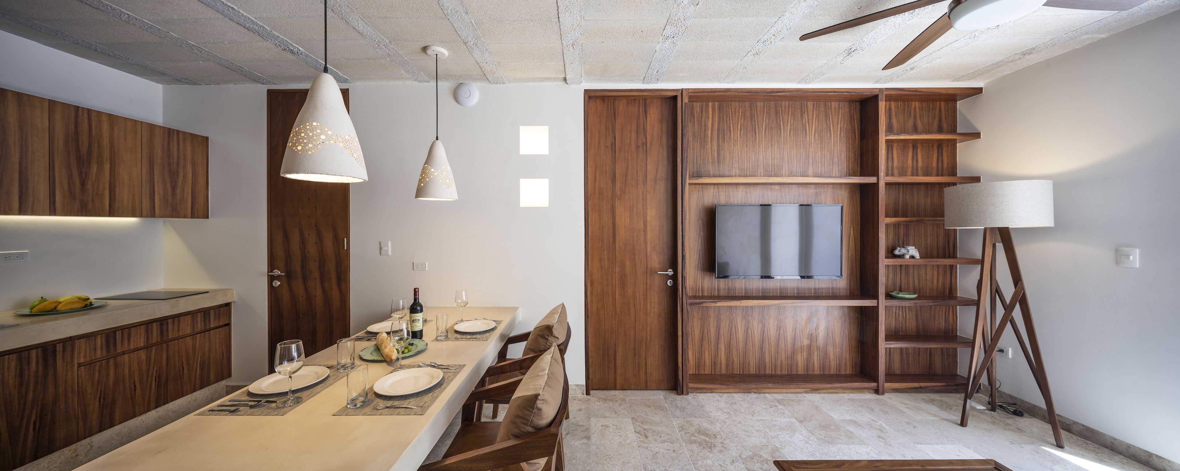 A modern kitchen with wooden cabinets, a dining table set for four, and a TV mounted on a wooden cabinet.