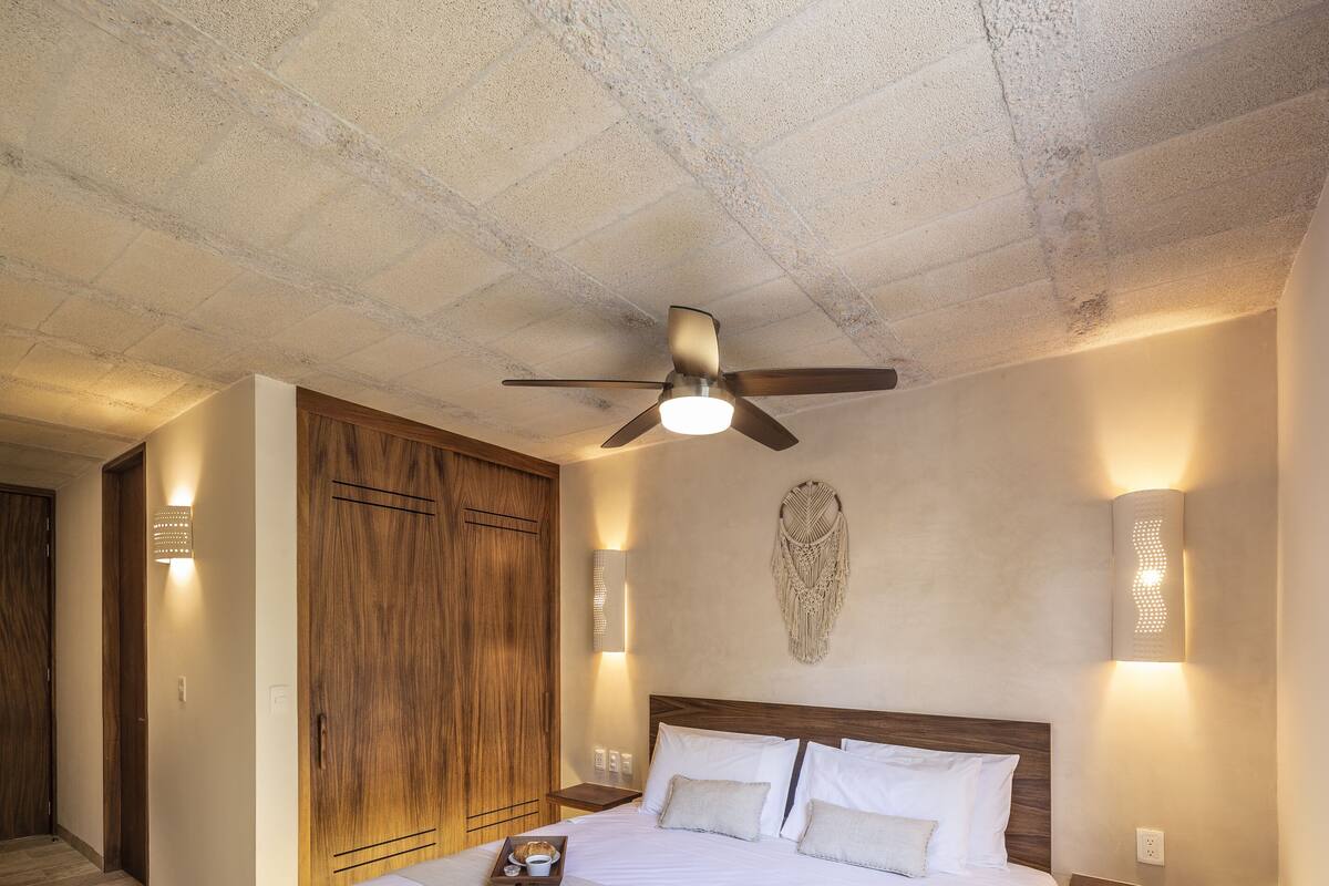 A spacious bedroom with a large bed, a ceiling fan, and wall-mounted lighting.