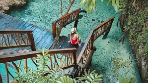 A wooden bridge leading to a clear blue pool surrounded by lush greenery. - Kiki Tulum (Tulum)