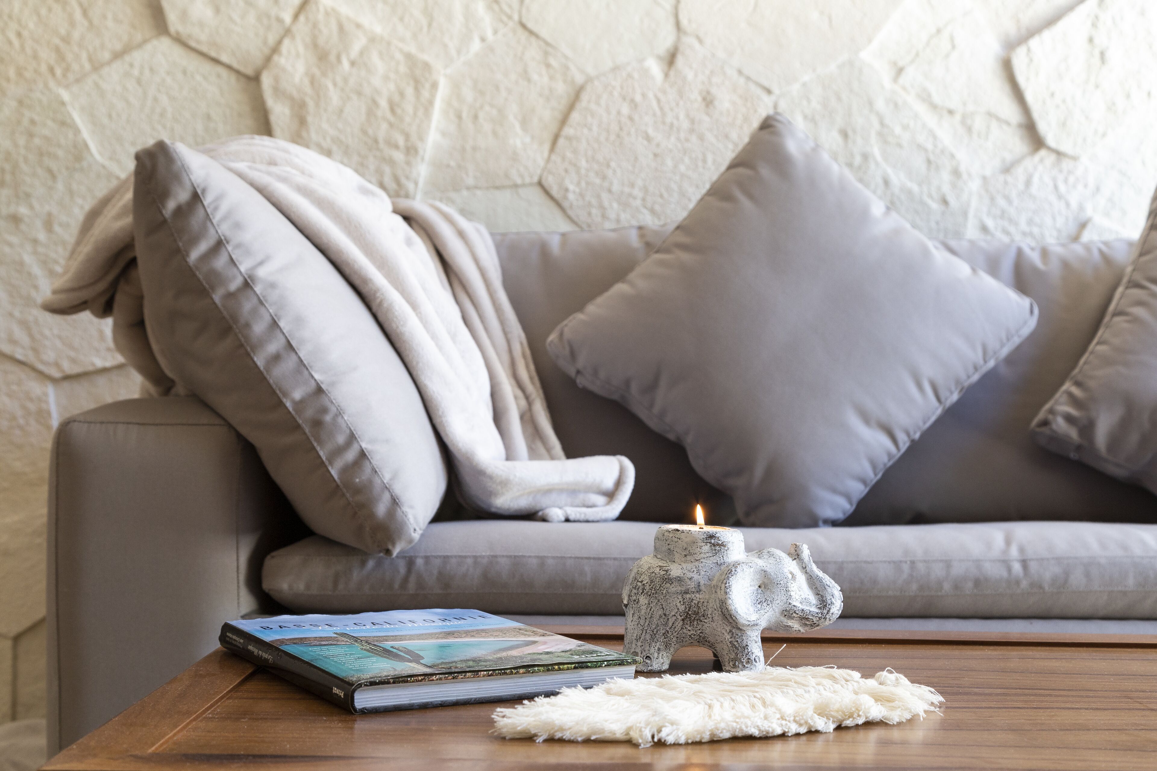 A living room with a grey sofa, a book, a small elephant figurine, and a candle on a wooden table.