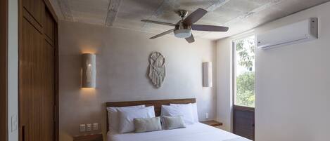 Une chambre dotée d’un grand lit, d’un ventilateur de plafond, d’un climatiseur mural et d’une fenêtre donnant sur un paysage verdoyant.