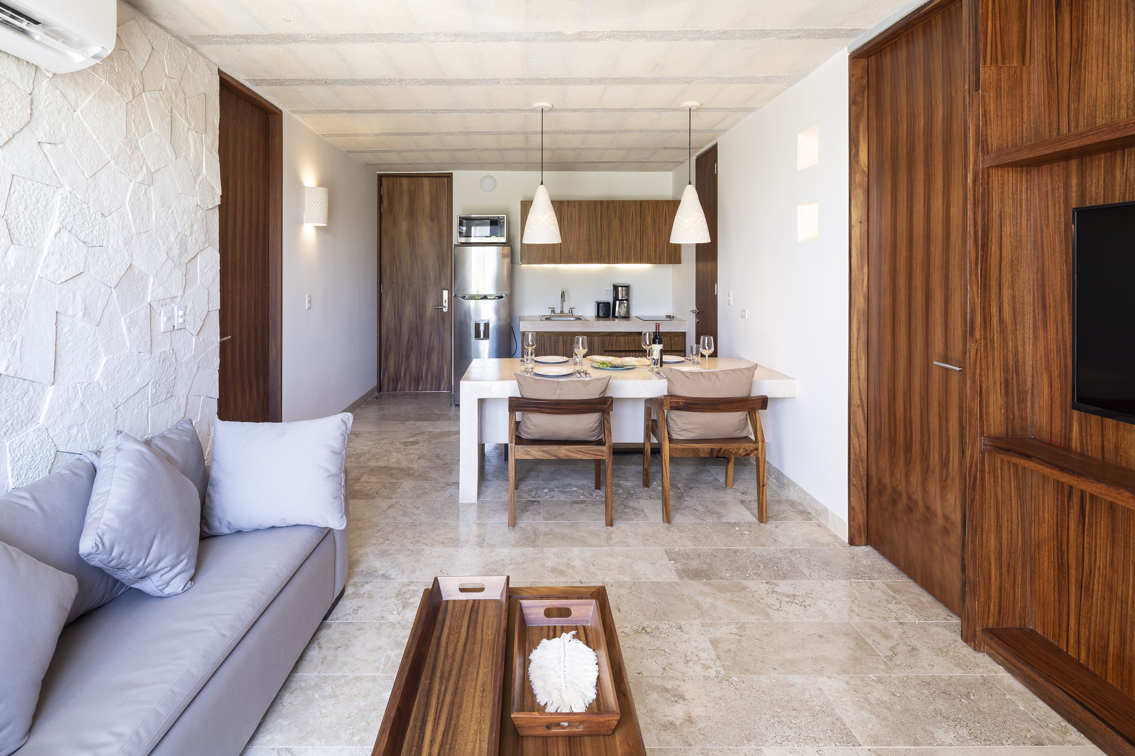 Una sala de estar moderna con un sofá, una mesa de comedor y sillas. Se observa un área de cocina al fondo con un refrigerador y una máquina de café.