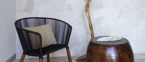 A room with a stone wall, a black woven chair with a cushion, and a wooden table with a branch decoration.