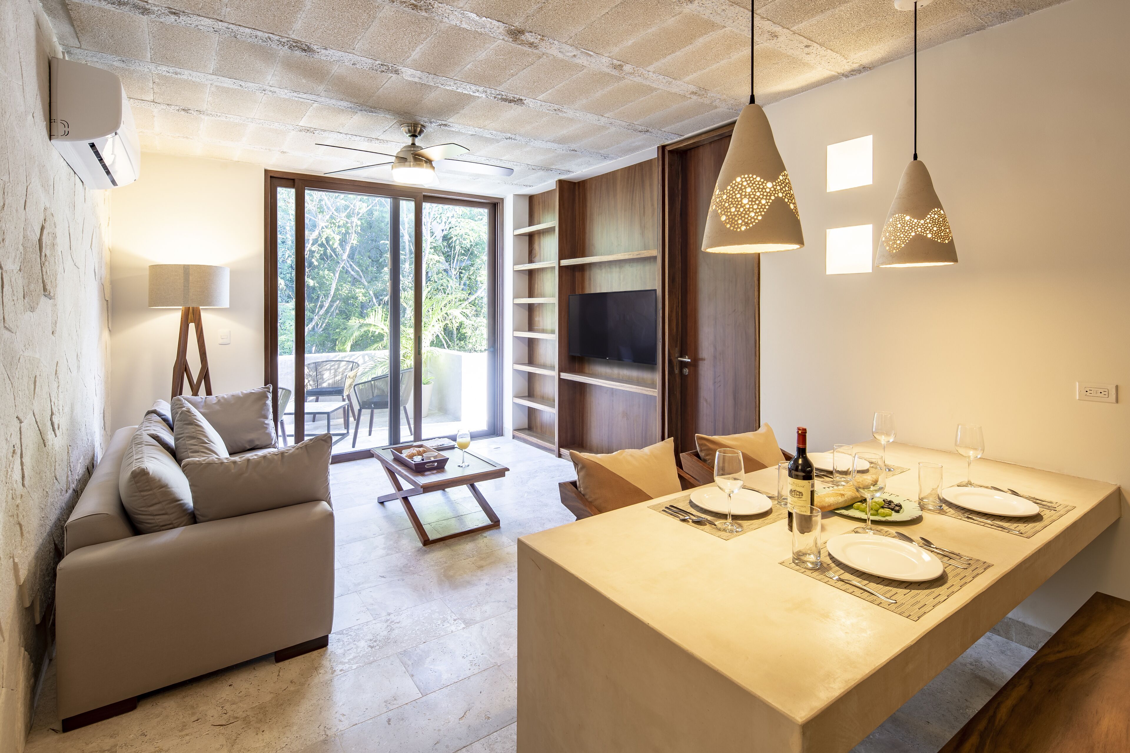A modern living room with a sofa, a dining table set for two, and a TV mounted on the wall.