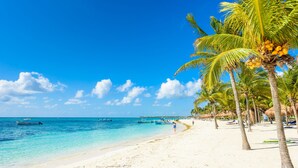 A beach with white sand, clear turquoise water, and palm trees. - Kiki Tulum (Tulum)
