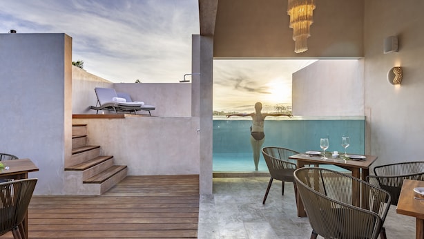 A modern outdoor area with a wooden deck, a lounge chair, a table with chairs, and a view of the pool. - Kiki Tulum (Tulum)