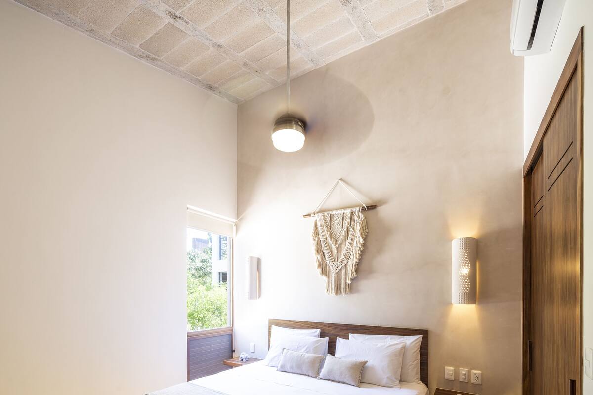 A spacious bedroom with a large bed, a ceiling fan, and a view of greenery outside.