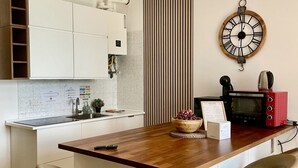 Een moderne keuken met witte kasten, een houten aanrecht, een klok, een magnetron en een mand met fruit.