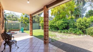 A covered patio area with a brick column, a table with chairs, and a view of a lush garden. - Lorikeet Retreat, 2/117 Tomaree Rd -  Pet Friendly, Air Conditioned Holiday House (Shoal Bay)