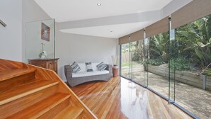 Un interno moderno con una scala in legno, un divano curvo con cuscini decorati e un'ampia vetrata che si affaccia su un giardino.