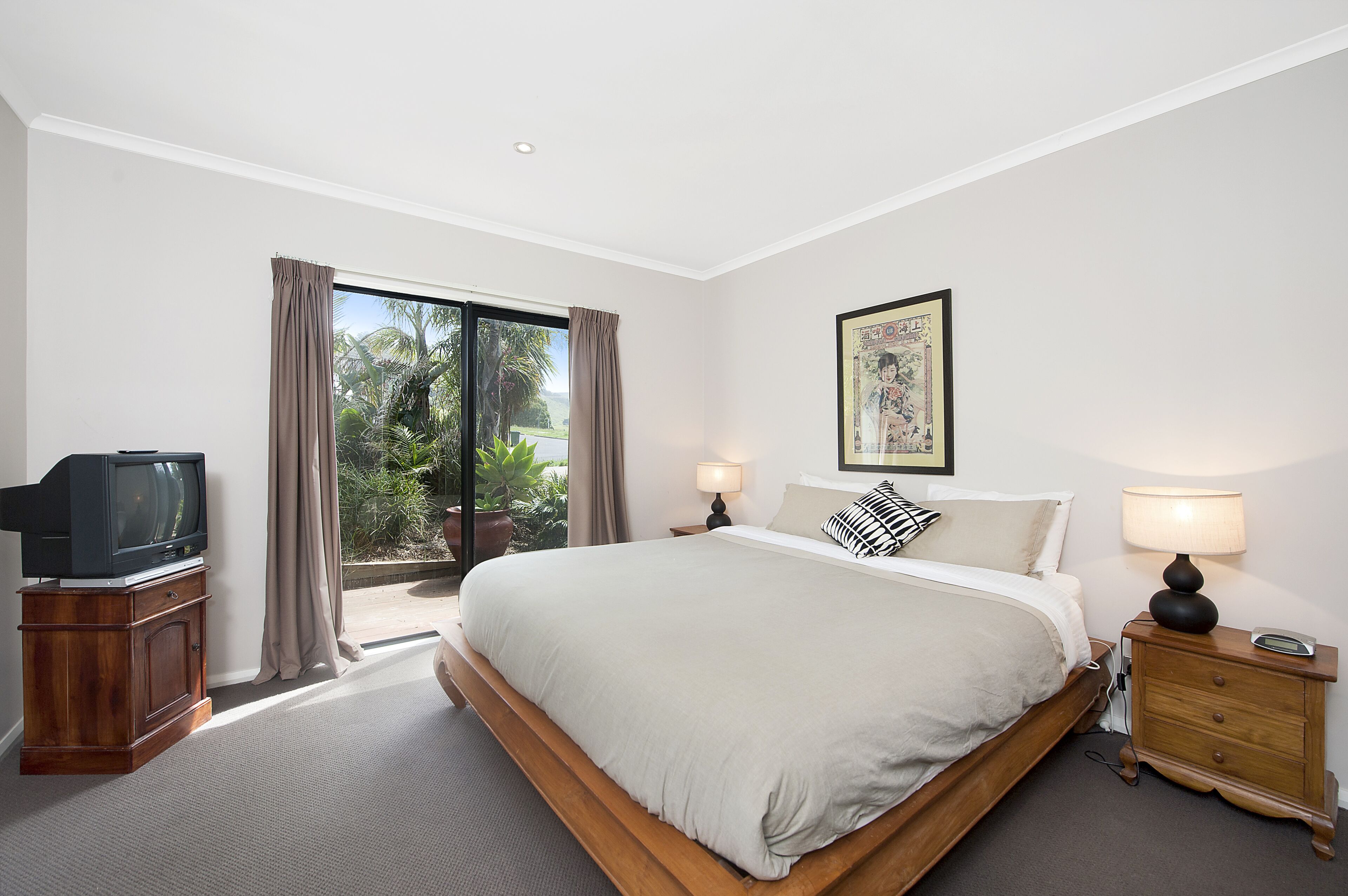 A bedroom with a large bed, a television on a wooden cabinet, a nightstand with a lamp, and a window with curtains.