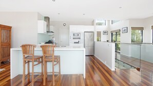 Una cucina moderna con mobili bianchi, un'isola centrale con due sgabelli in legno e una ringhiera in vetro che si affaccia su un balcone.