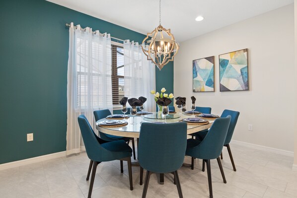 Un coin repas avec une table ronde, des chaises bleues, un lustre et une œuvre d’art abstraite accroch ée au mur.
