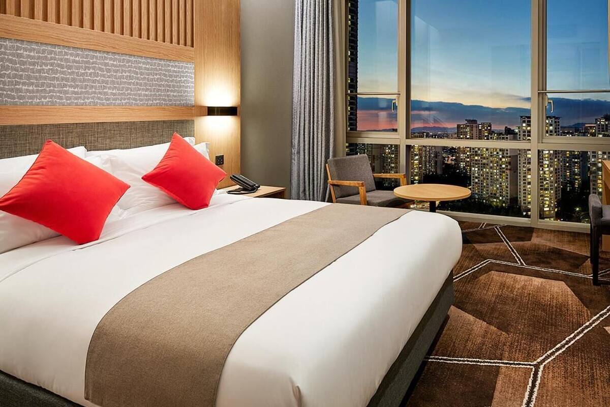 A hotel room with a large bed, a city view, a small table, and a chair.