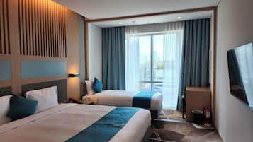 A hotel room with two beds, a large window with curtains, a flat-screen TV, and a fire extinguisher.