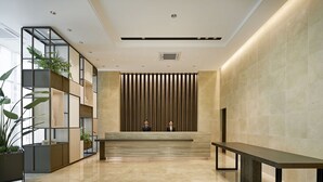 A modern lobby with a reception desk, two seated individuals, and a large potted plant. - Staz Hotel Premier Dongtan (Hwaseong)