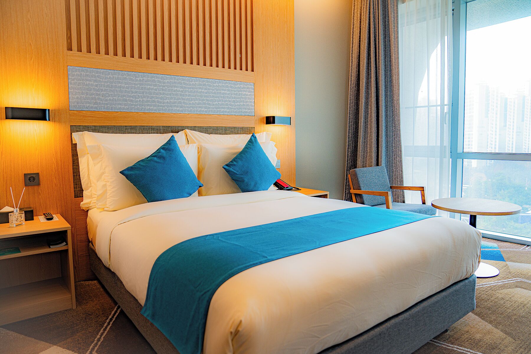 A hotel room with a large bed, a bedside table, a chair, and a small table.