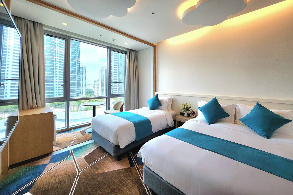 A hotel room with two beds, a view of tall buildings, and a modern design.