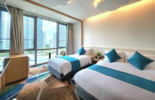 Habitación de hotel con dos camas, un escritorio y un ventanal que ofrece vistas a la ciudad.