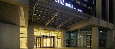 L’extérieur du STAZ HOTEL PREMIER se distingue par sa façade en verre, son entrée imposante et les flèches directionnelles peintes sur le trottoir.