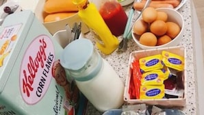 Una mesa con diferentes alimentos y condimentos, como Kellogg's Corn Flakes, huevos, perritos calientes y mostaza.