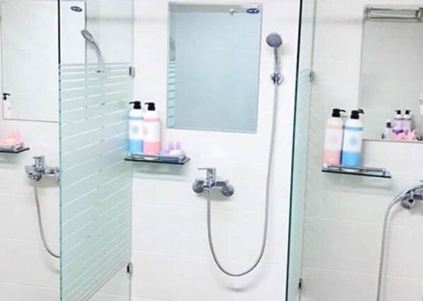 Un baño con mamparas de vidrio en la ducha, un espejo y repisas con artículos de aseo.