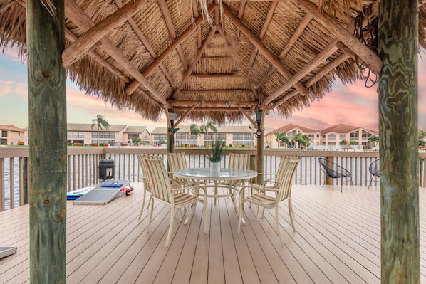 A covered outdoor area with a thatched roof, wooden deck, and a table with chairs.