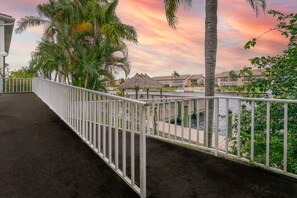 A waterfront balcony with a white railing, palm trees, and a thatched-roof structure.