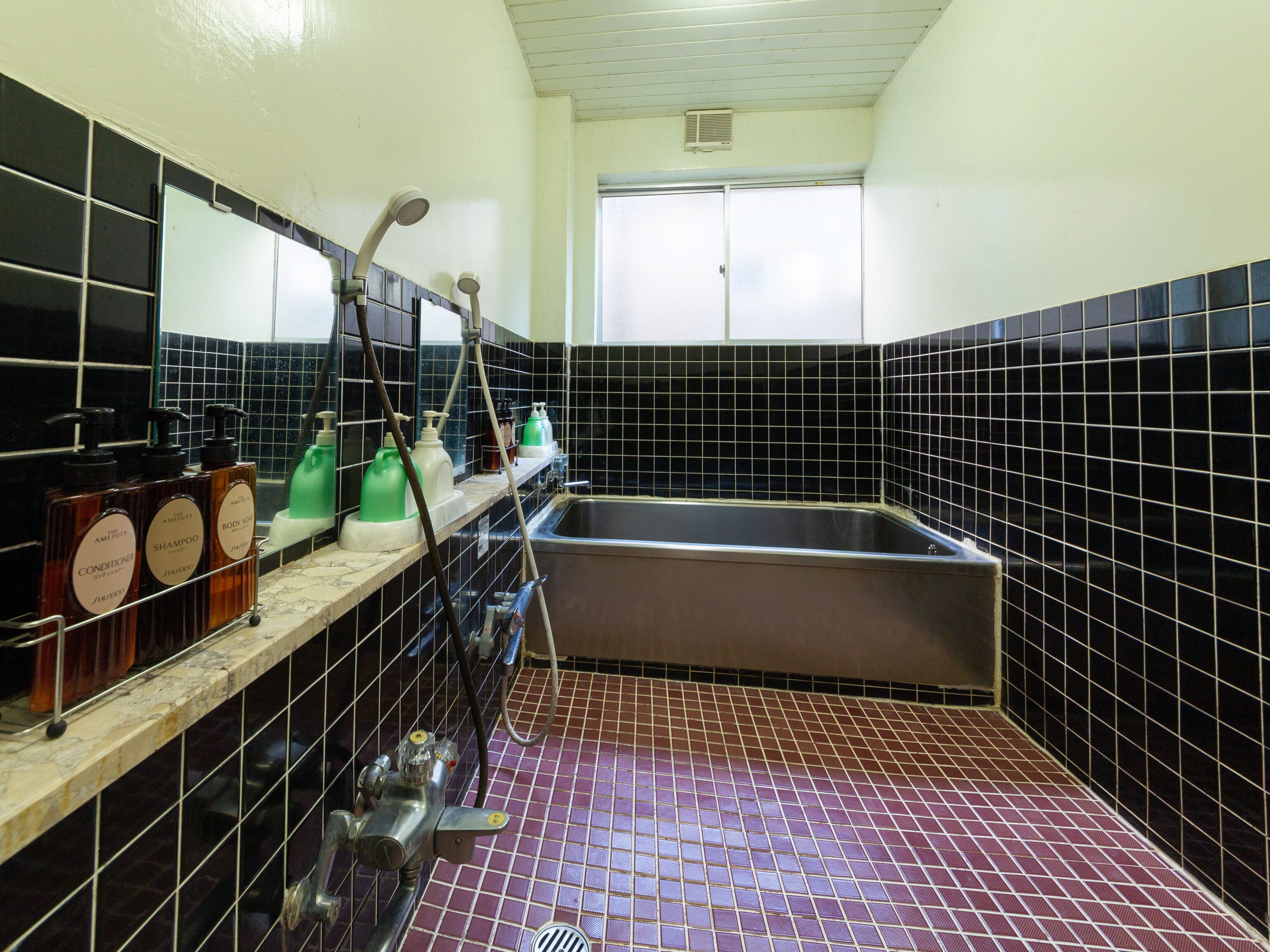 A bathroom with black tiled walls, a large sink, and shelves holding toiletries.