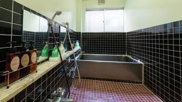 A bathroom with black tiled walls, a large sink, and shelves holding toiletries.