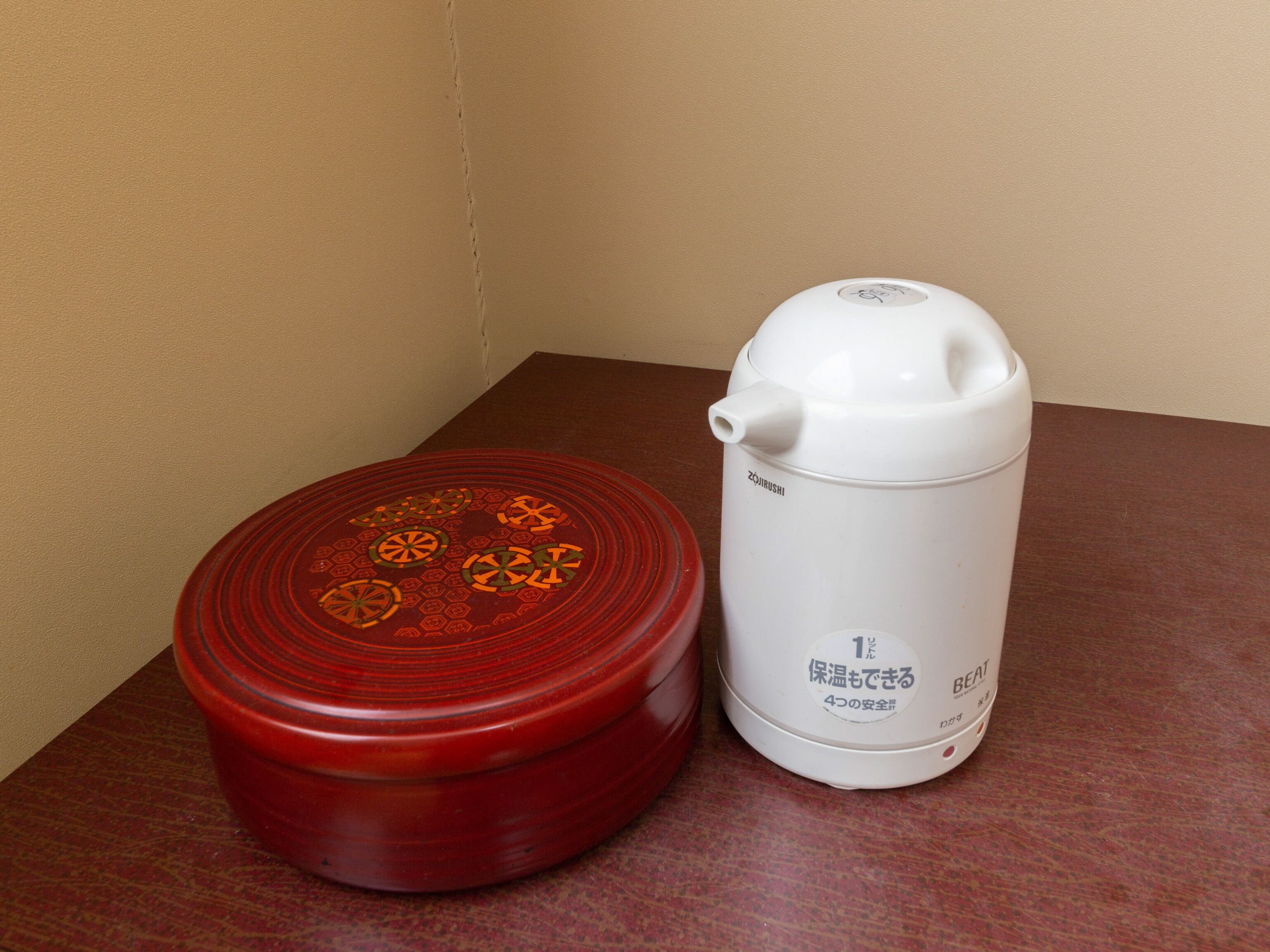 A red container with a lid and a white electric kettle on a wooden table.