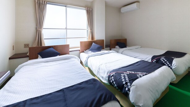A hotel room with two single beds, a window with curtains, an air conditioning unit, and a green carpet. - Tabist Business Hotel Chitose Kashiwazaki (Kashiwazaki)