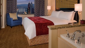 A hotel room with a large bed, a blue armchair, a view of the city skyline, a patterned headboard, and a marble countertop with a sink. - Master Bedroom at Marriott Grand Chateau (Las Vegas)