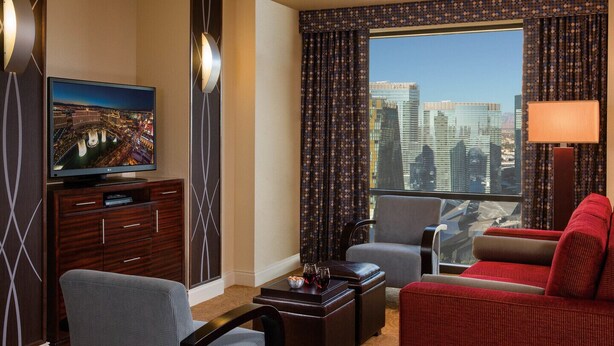 A hotel room with a television, a sofa, a chair, a coffee table, and a view of a cityscape. - Master Bedroom at Marriott Grand Chateau (Las Vegas)
