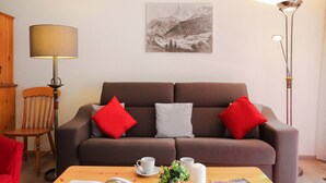 Ein modernes Wohnzimmer mit einem braunen Sofa, roten und grauen Kissen, einem Holzstuhl, einem Couchtisch mit einem Buch, einer Kerze und einer Zeitschrift.