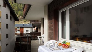 Ein Balkon mit Tisch für zwei Personen, einem Korbwicker-Korb mit Früchten und Blick auf eine Berglandschaft.