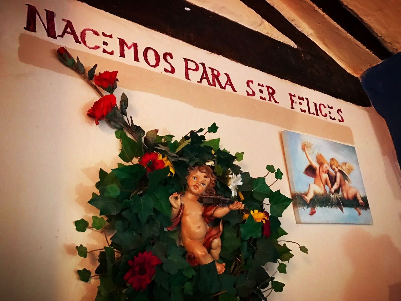 A wall with a decorative arrangement including a cherub figure surrounded by foliage and flowers, and a painting of cherubs.