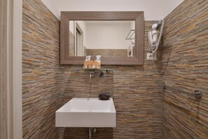 Un baño con un lavamanos rectangular, un espejo sobre él y una zona de ducha con un perchero.