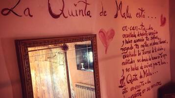 Un espejo con un marco decorativo refleja una habitación con ventana, un radiador y una inscripción en la pared.
