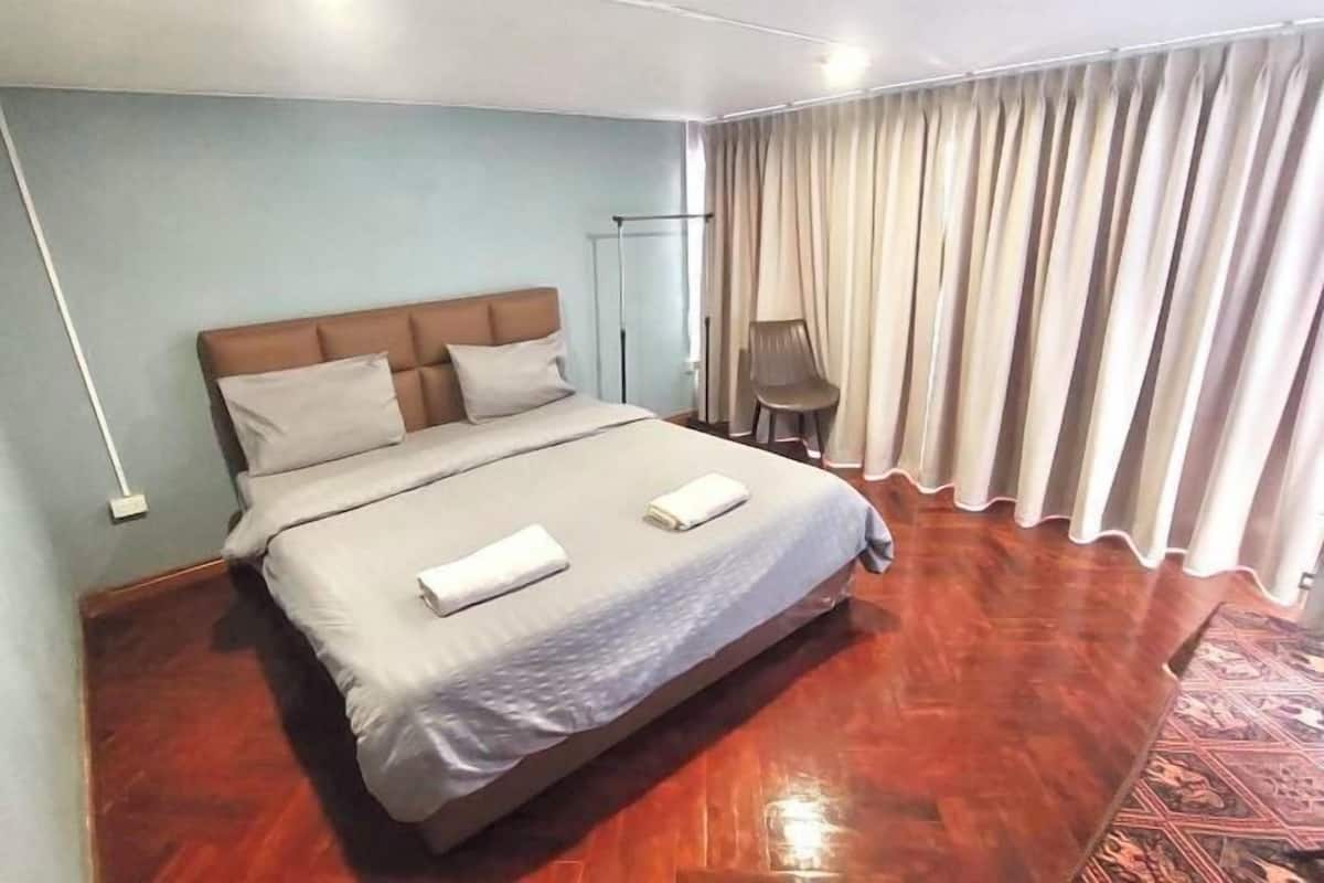 A hotel room with a bed, a chair, a standing lamp, and a curtain.