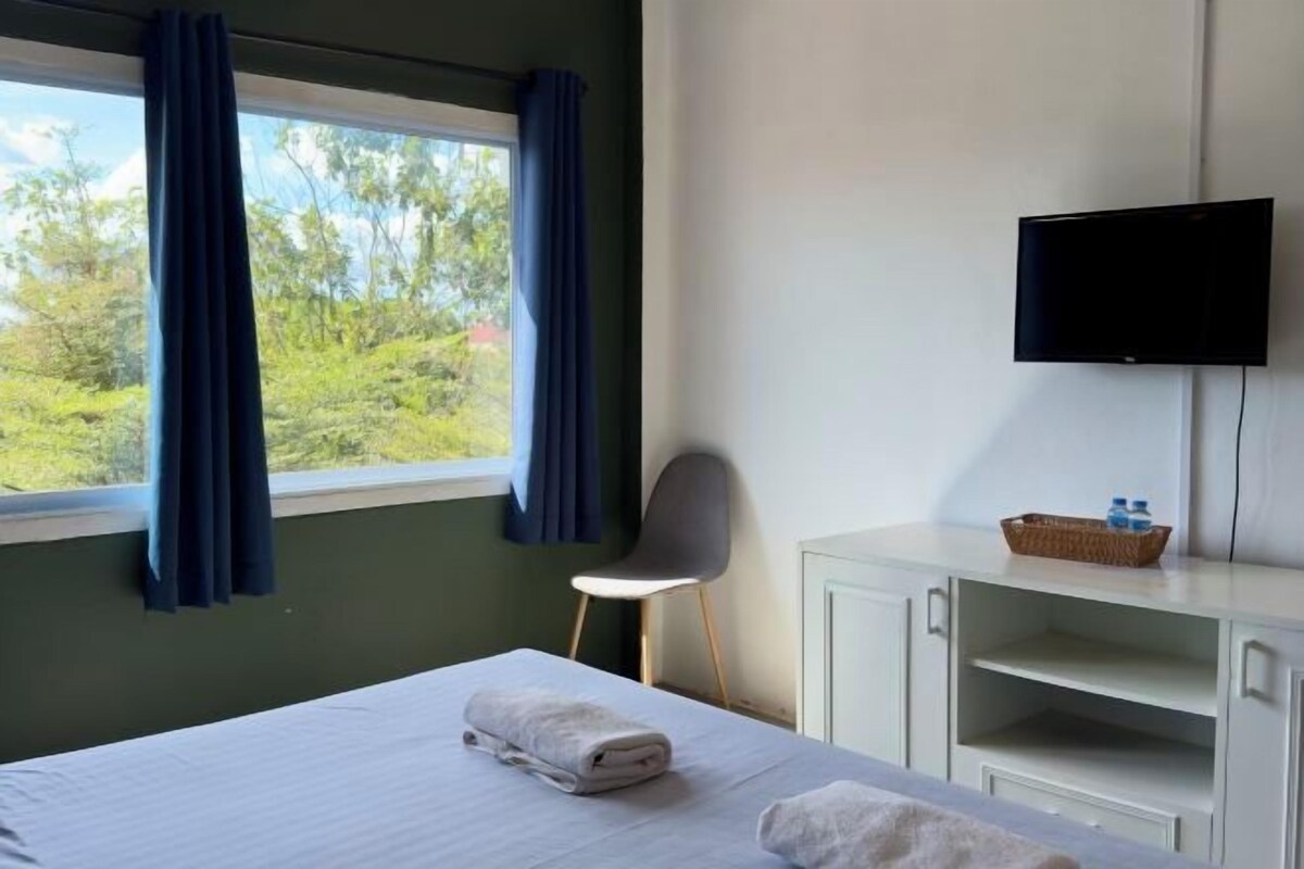 Hotellihuone, jossa on sänky, tuoli, televisio ja ikkuna, jossa on verhot.
