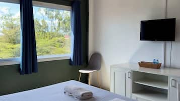 Habitación de hotel con cama, una silla, televisión y ventana con cortinas.